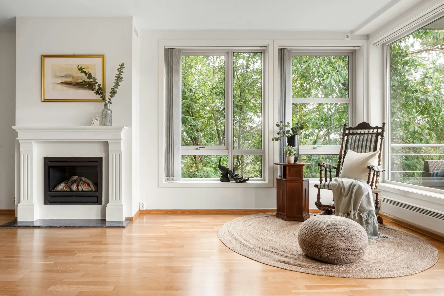 The living room, with a white fireplace, a rocking chair and three tall windows