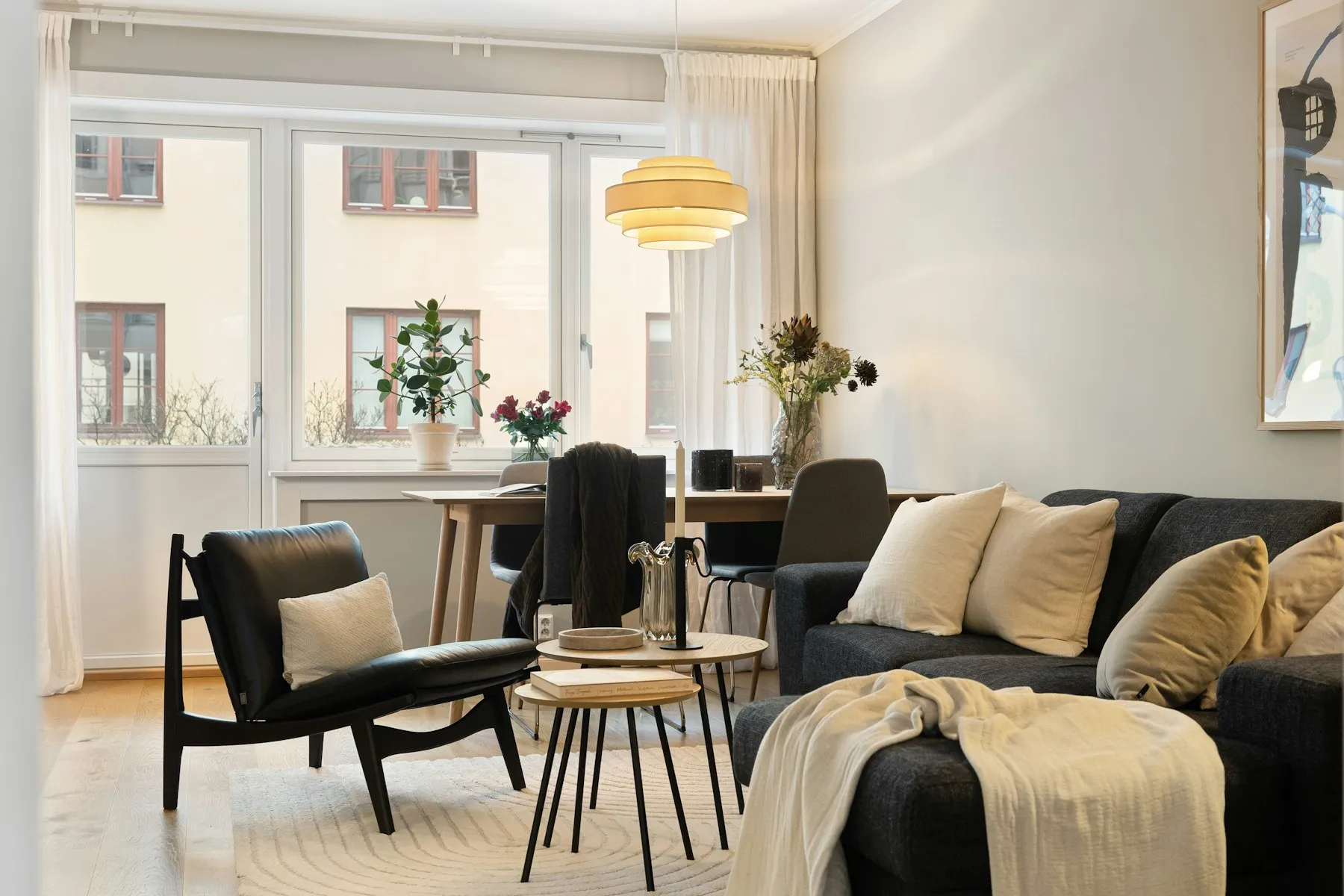 The living room, with a black sofa, a leather lounge chair and tall white windows