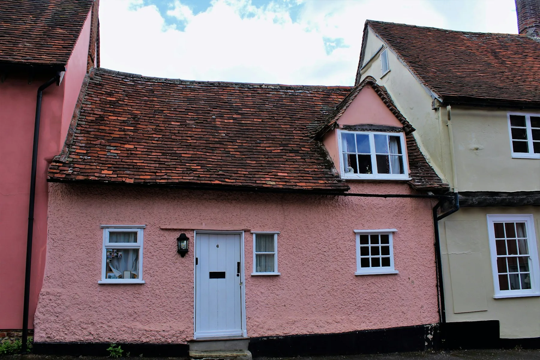 The front of the cottage, painted pink, with a tiled roof and a pale blue door
