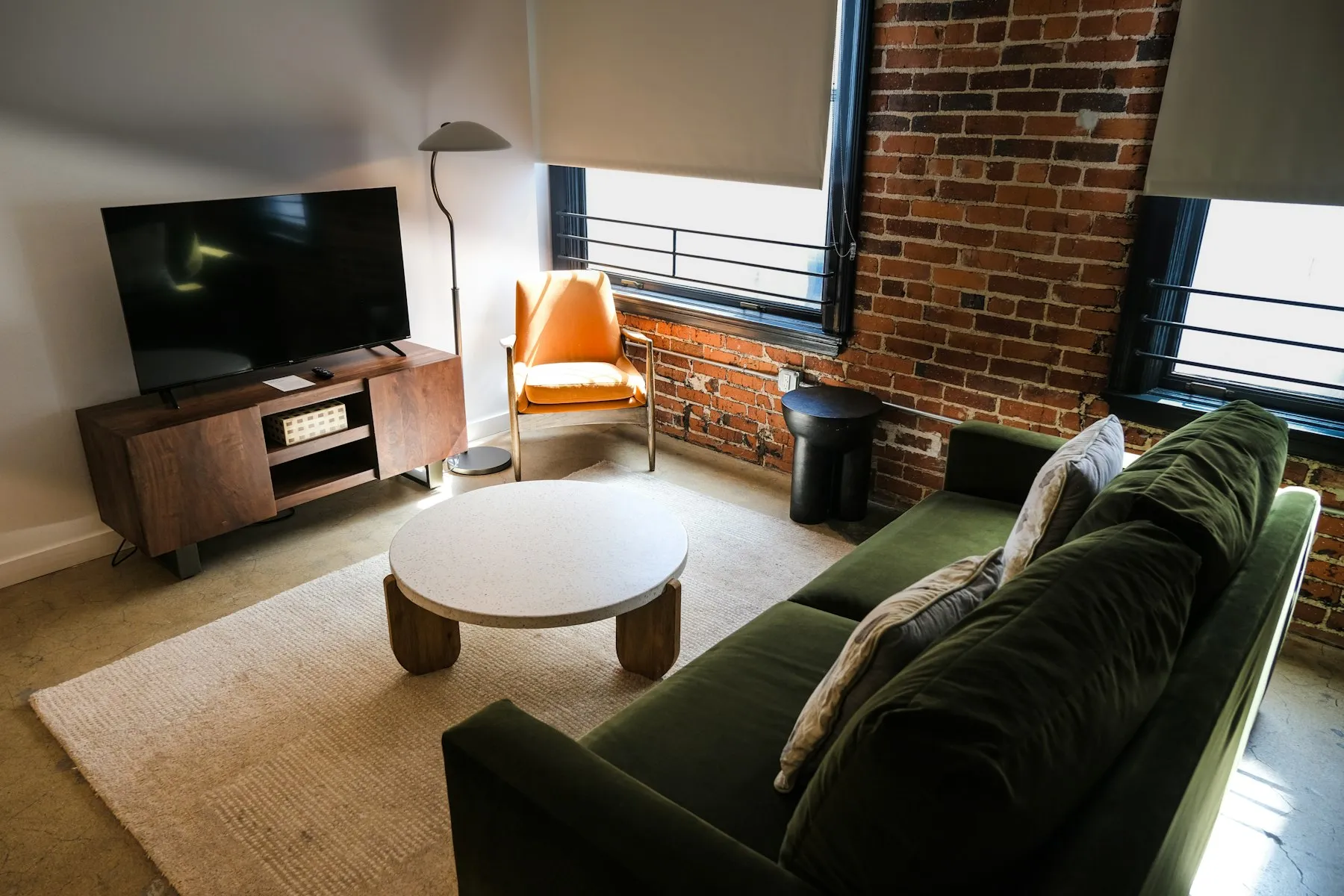 The living area, with a green velvet sofa, a round coffee table and a wall of exposed brick