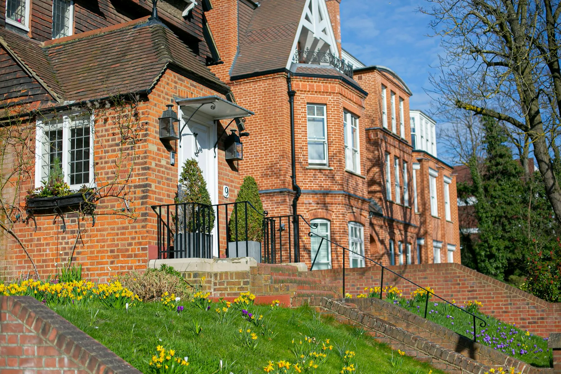 The red-brick front of the house, with tall chimneys, leaded windows and a garden of spring bulbs