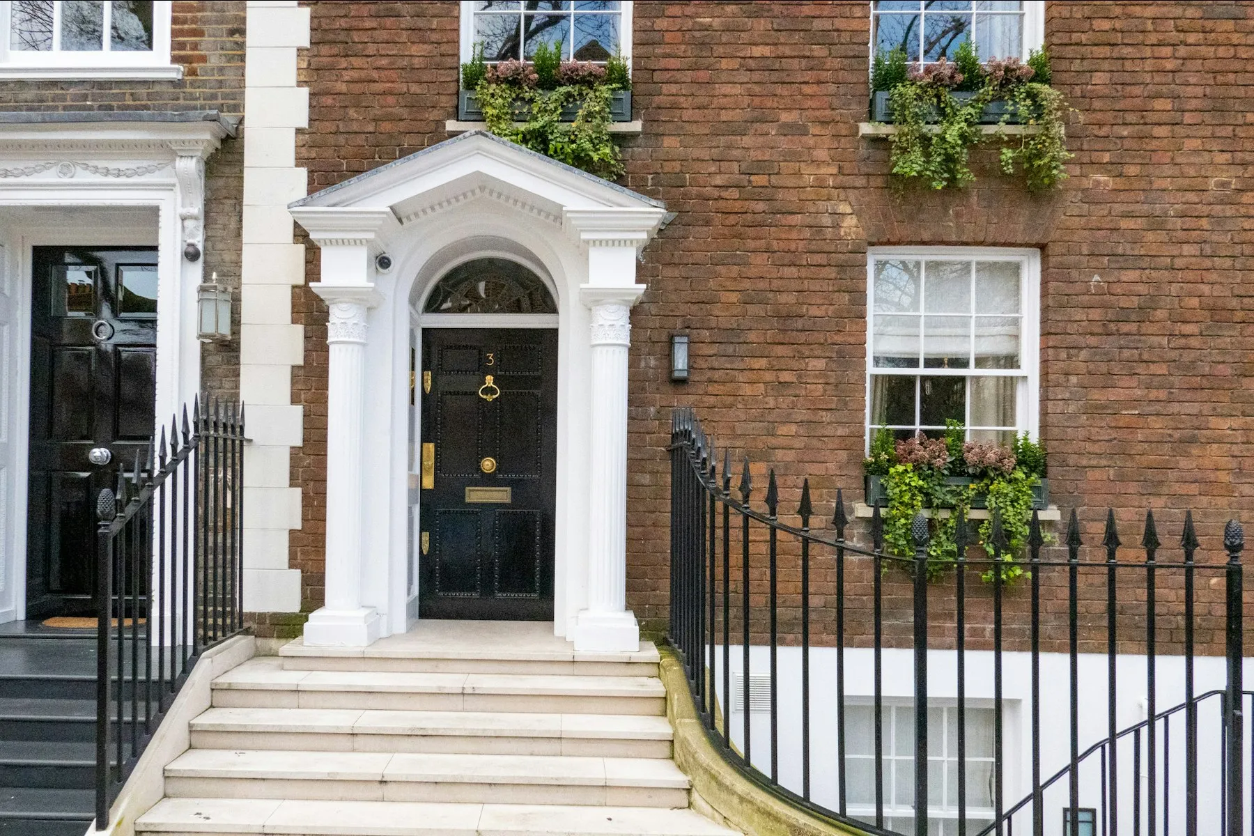 The brick façade of the townhouse, with a white pedimented doorcase, black front door and window boxes