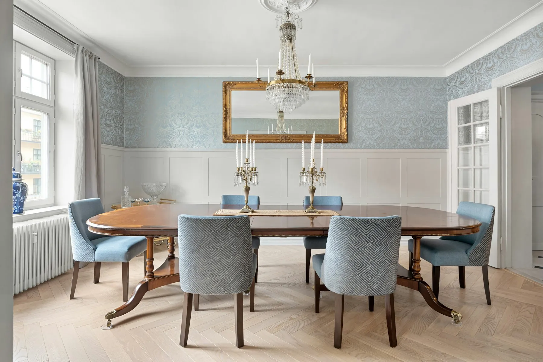 The dining room, with a polished wooden table, blue upholstered chairs and panelled walls