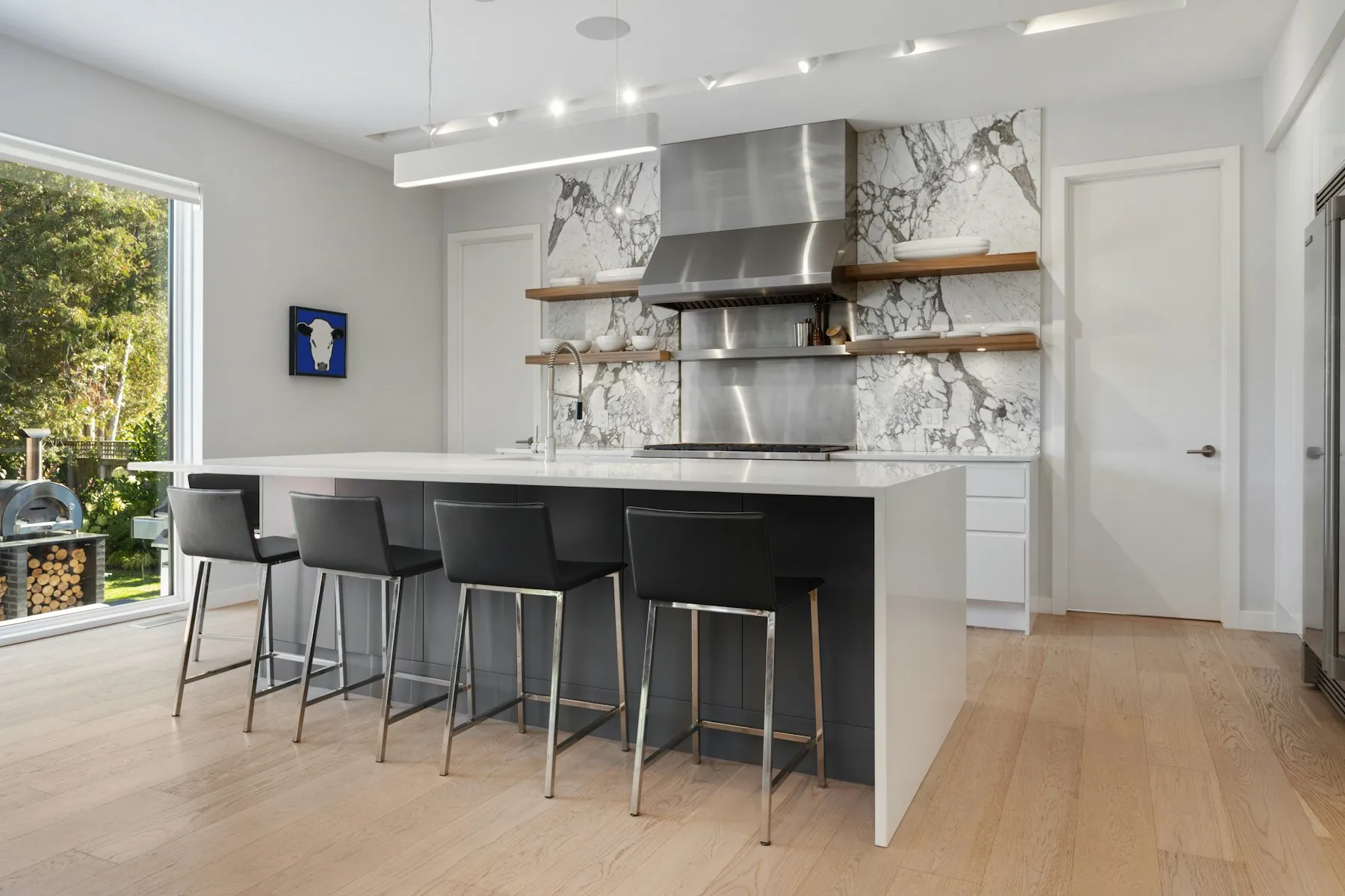 The kitchen, with a long white island, black bar stools and open shelves