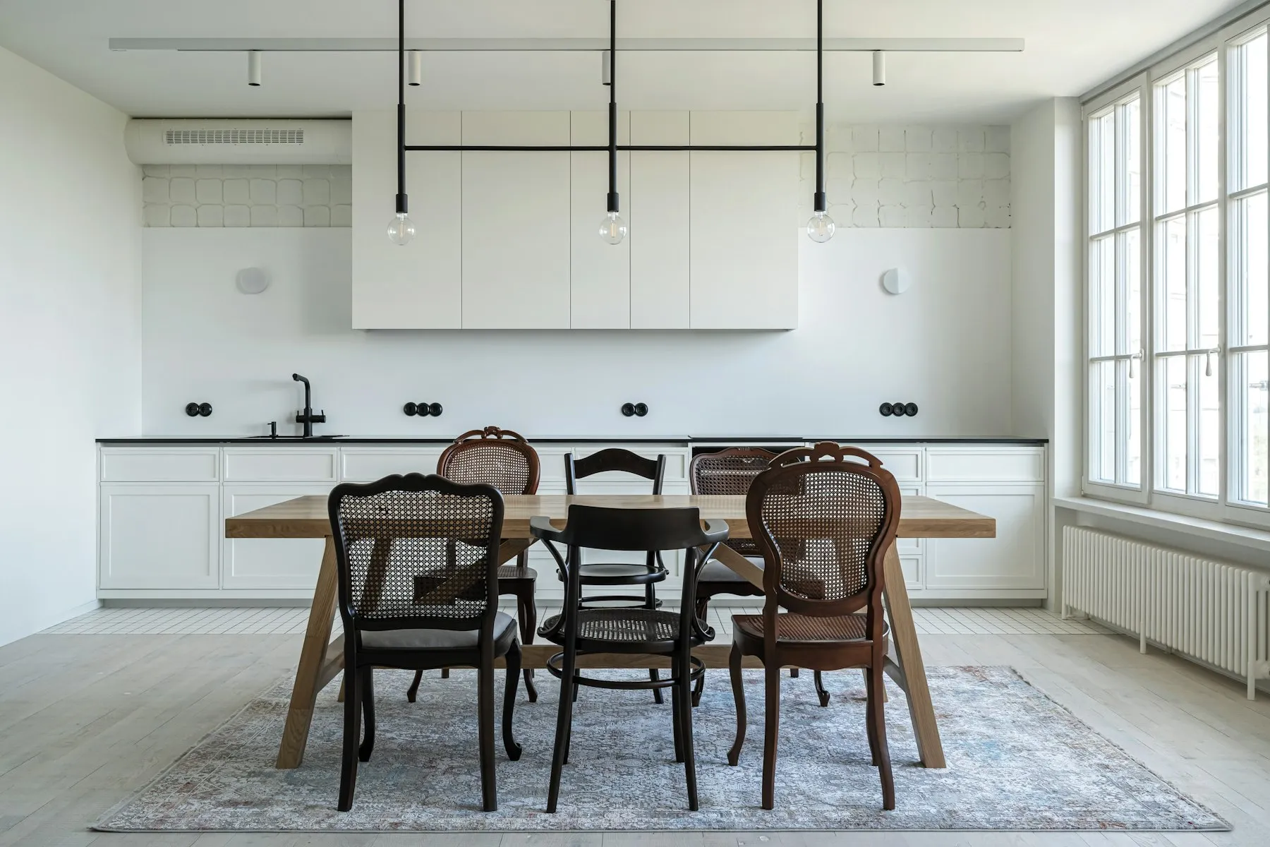 The kitchen, with white cabinets, an open shelf and a dining table with mismatched chairs