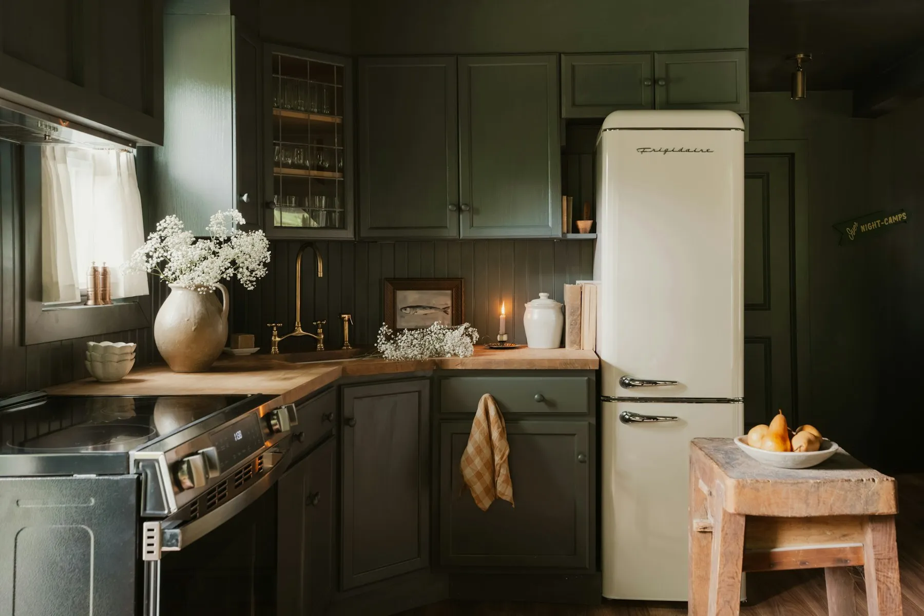 The kitchen, with dark green cabinets, a butcher's block and a cream fridge