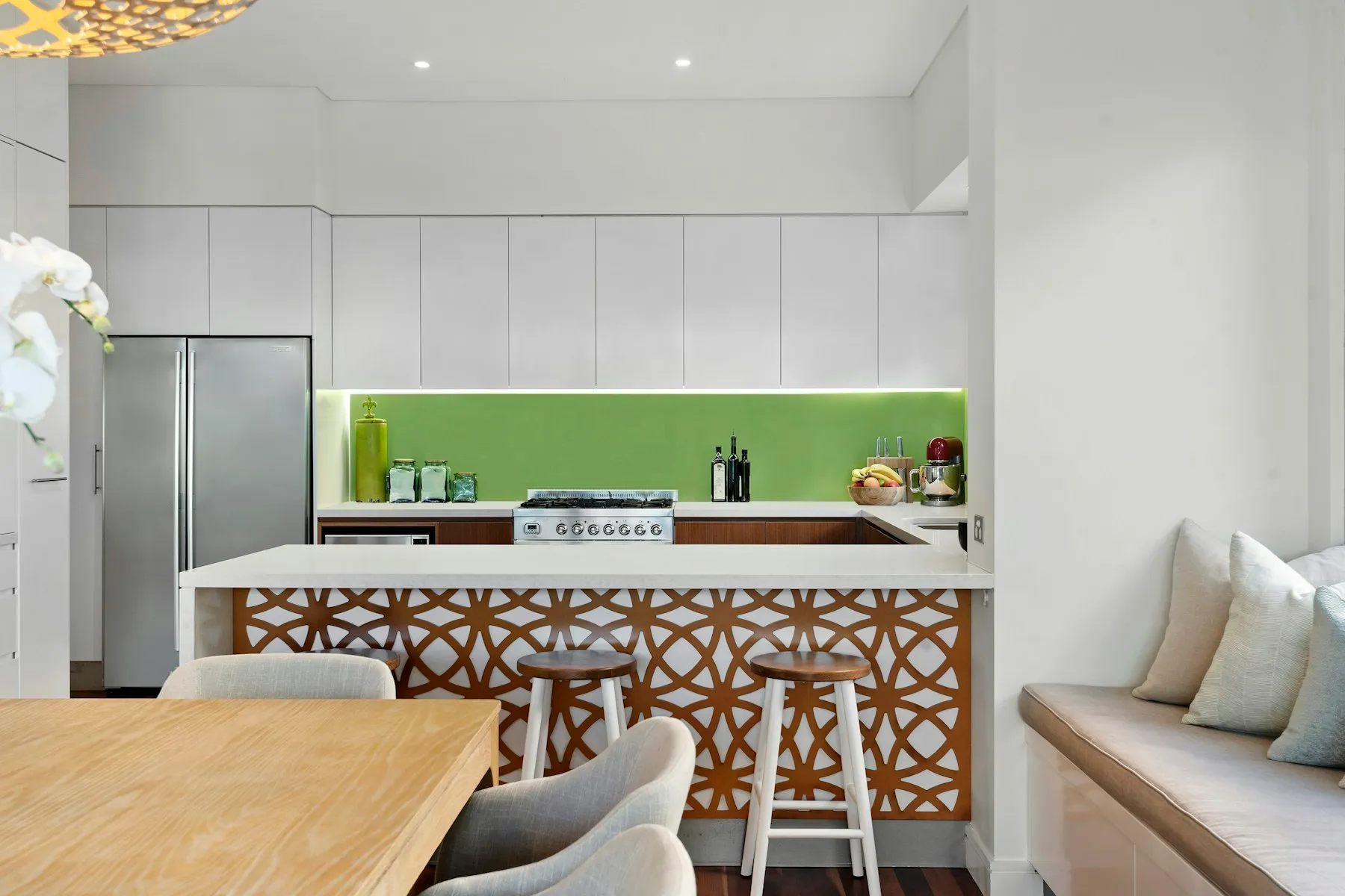 The kitchen, with white cabinets, a green glass splashback and a breakfast bar