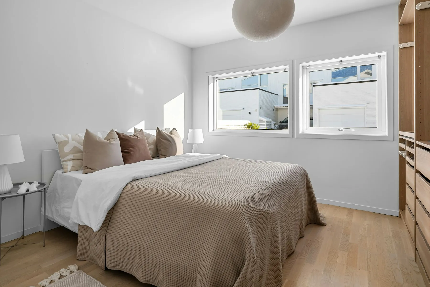 The principal bedroom, with a wide bed, taupe linens and two windows