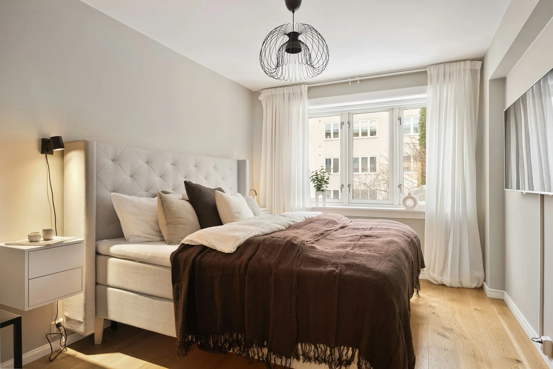The bedroom, with a padded headboard, brown throw and a pendant light