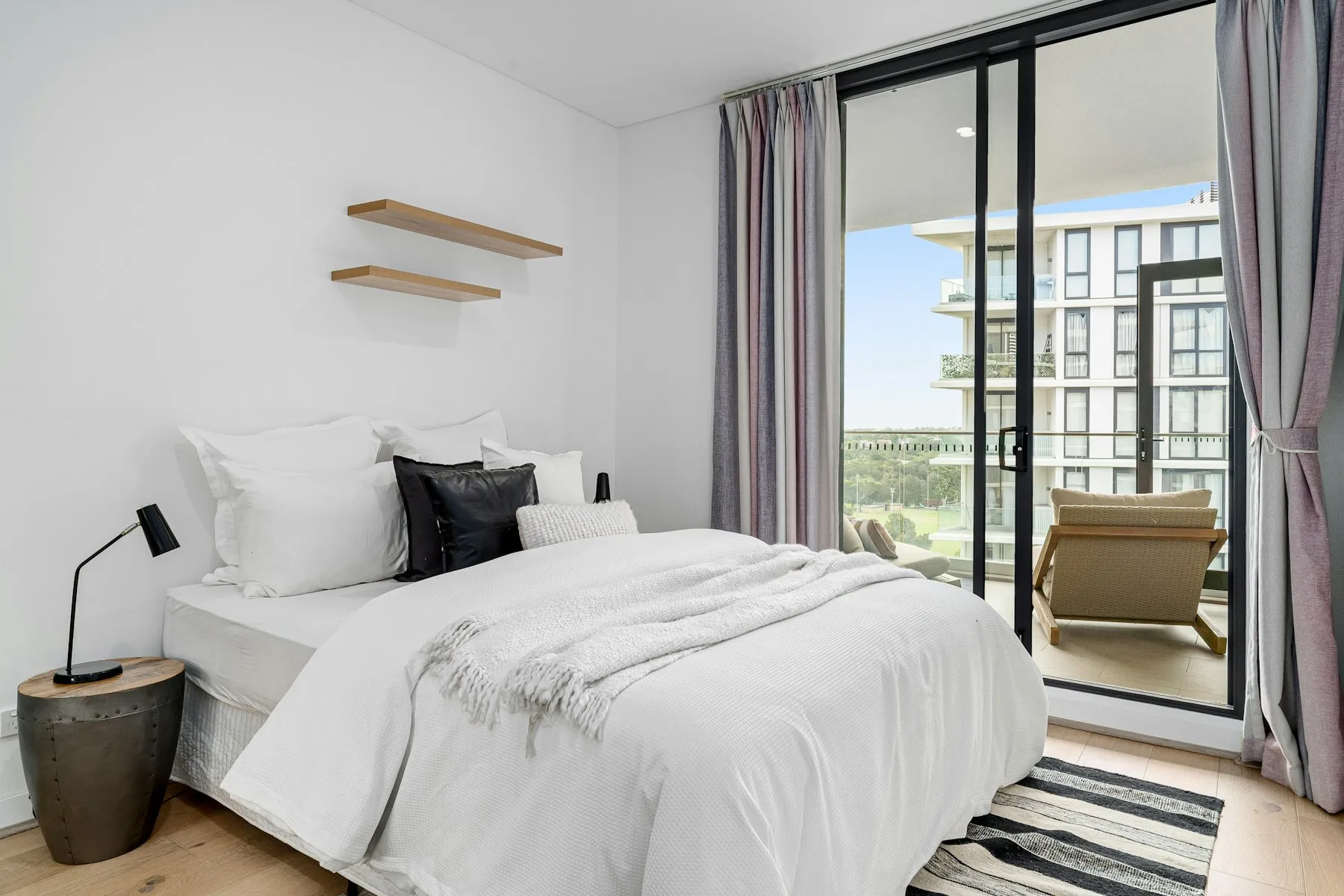 The bedroom, with white bedding and a door to the balcony