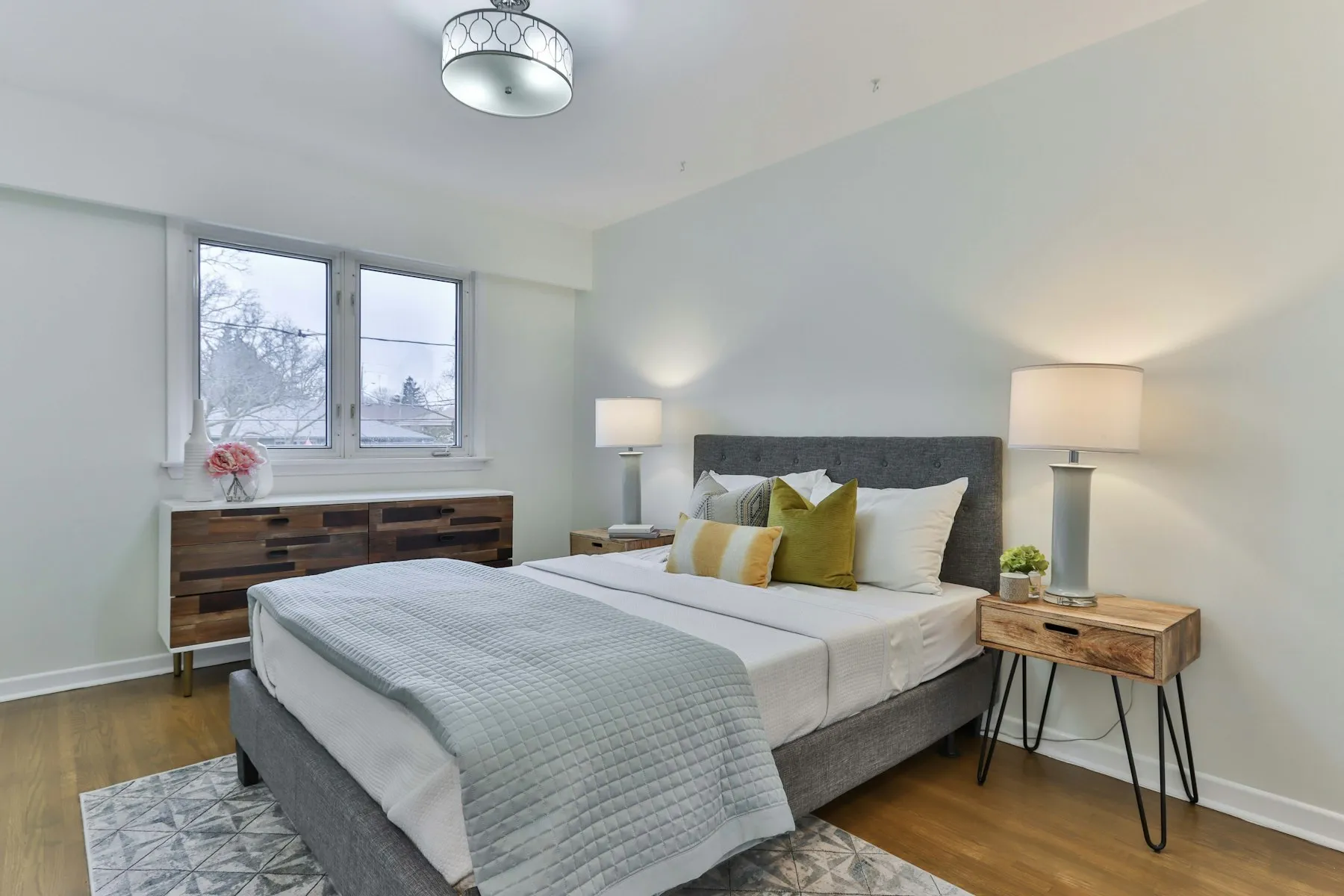 The principal bedroom, with a grey upholstered bed and a wooden chest of drawers
