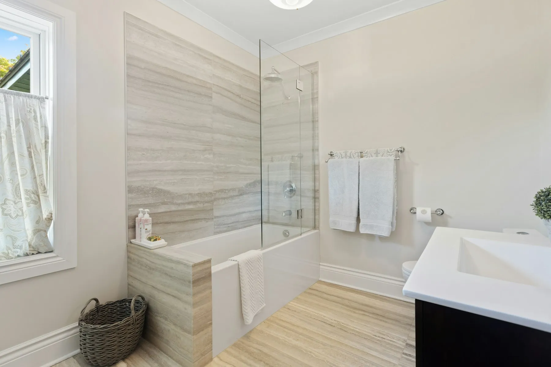 A bathroom lined in pale marble, with a bath and a separate basin