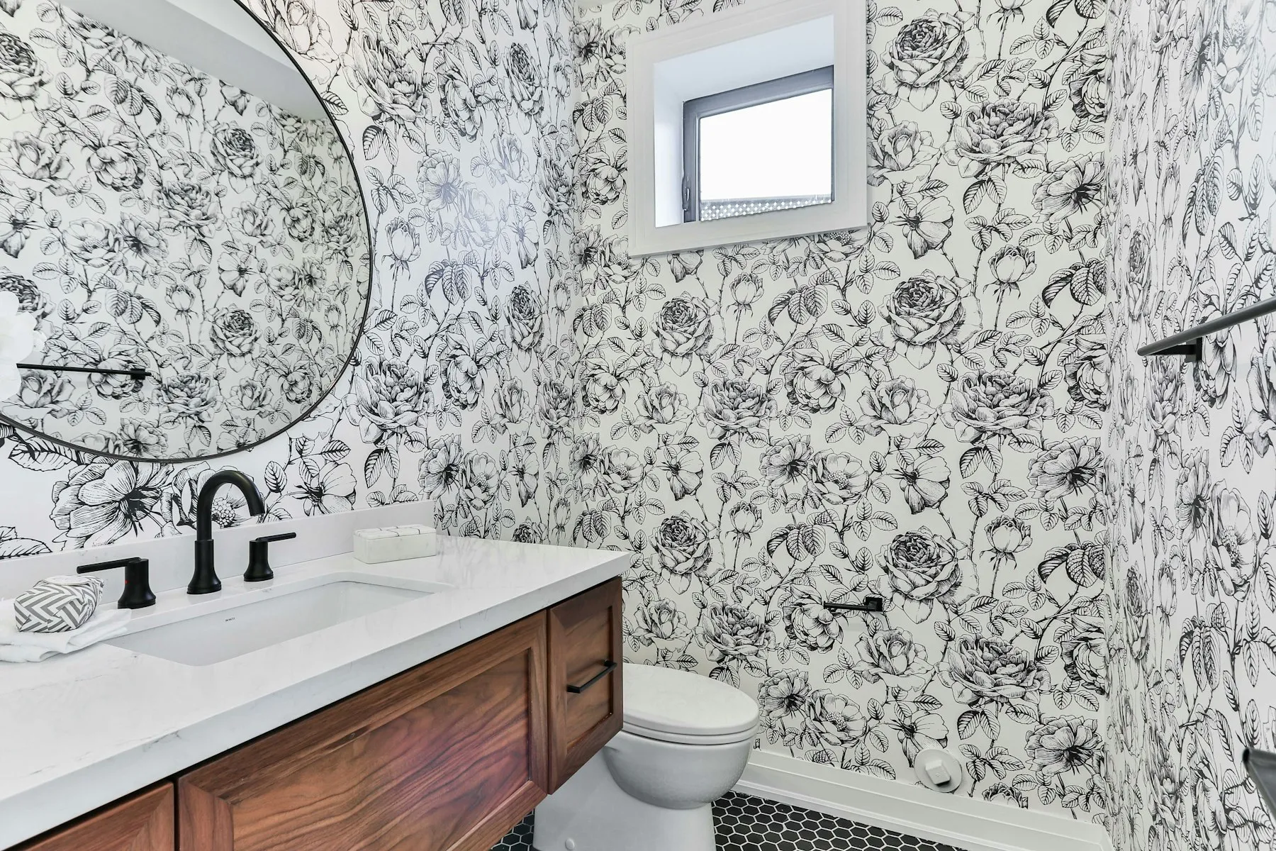 The cloakroom, with botanical wallpaper, a round mirror and a walnut vanity