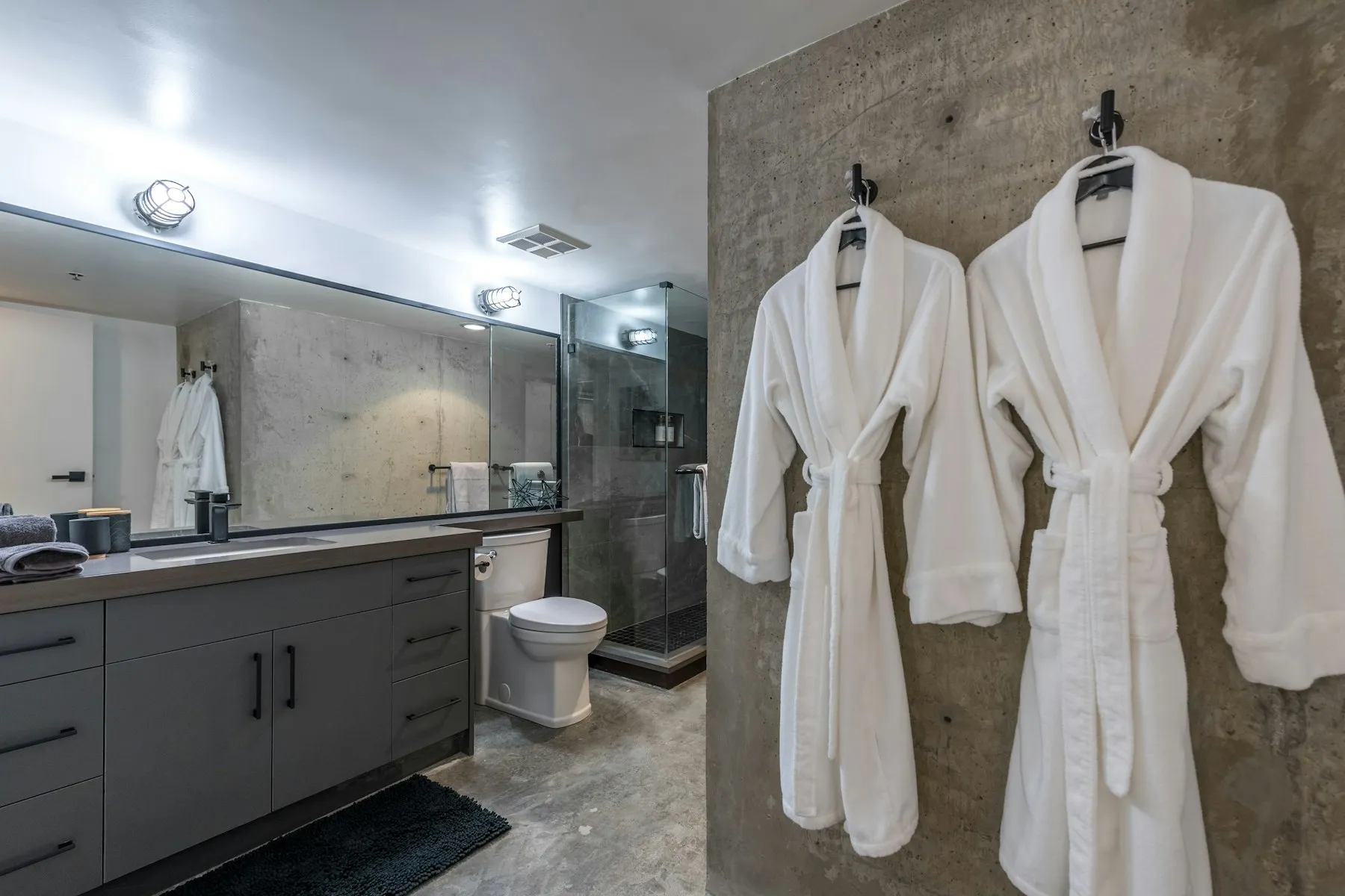 The shower room, with concrete-effect walls and two white bathrobes on hooks