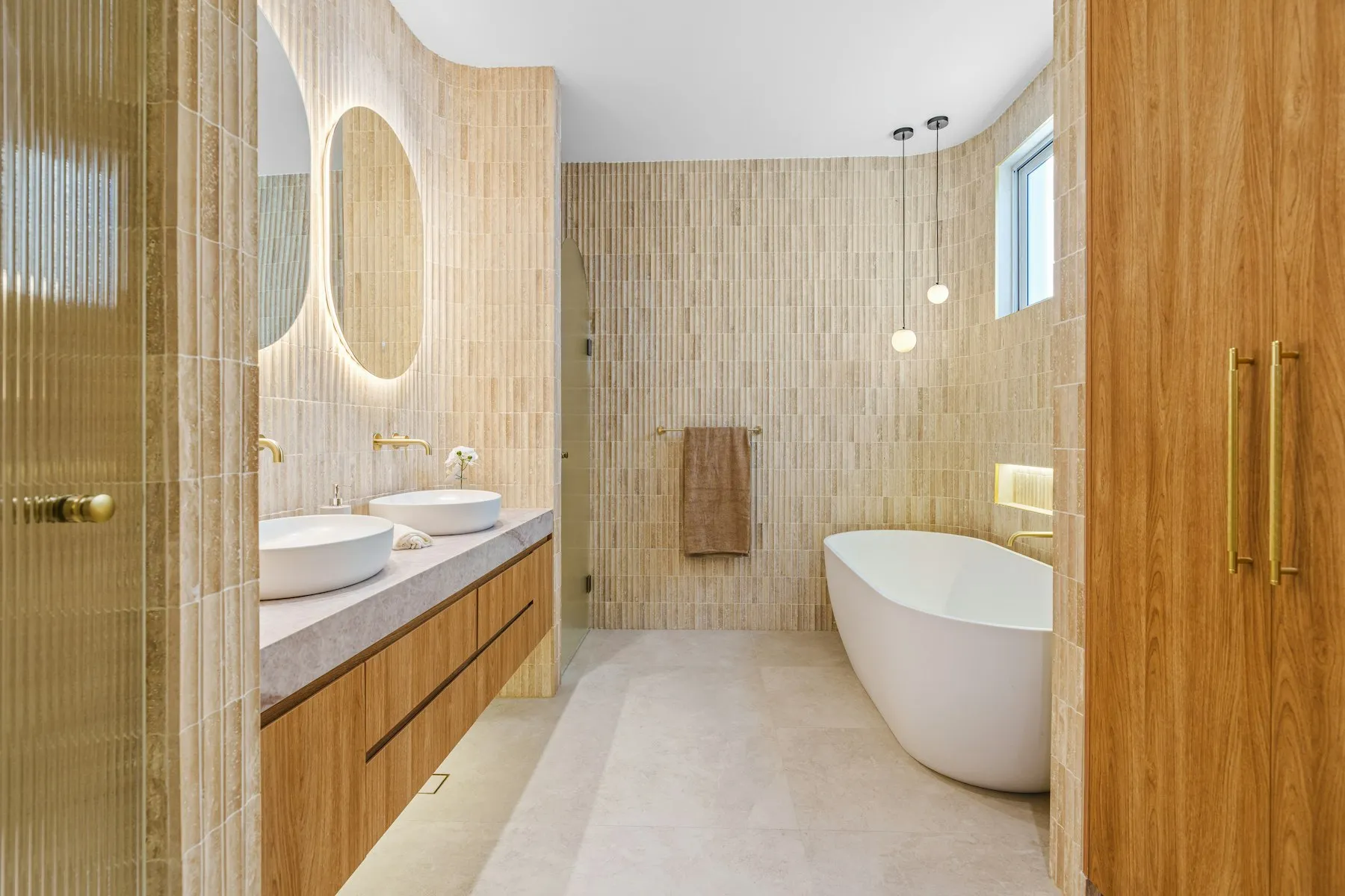 The en suite, with a freestanding bath, a stone-effect wall and a backlit mirror