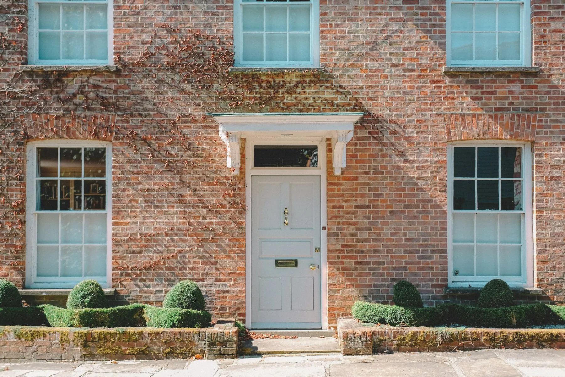 A red-brick Georgian house front with a grey-blue door under a white pediment and a box-hedged front garden