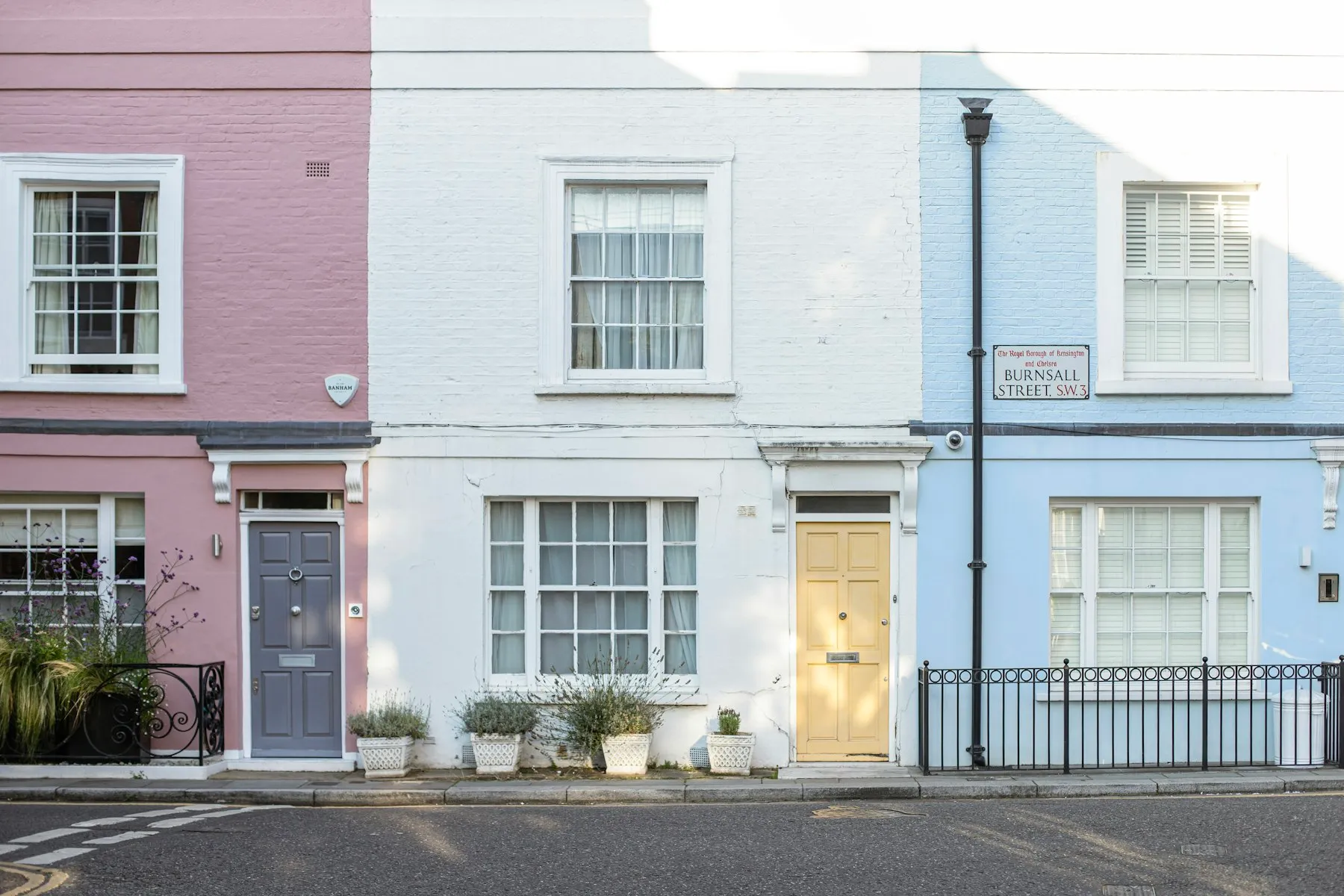 Small pastel-painted terraced houses with sash windows and black railings
