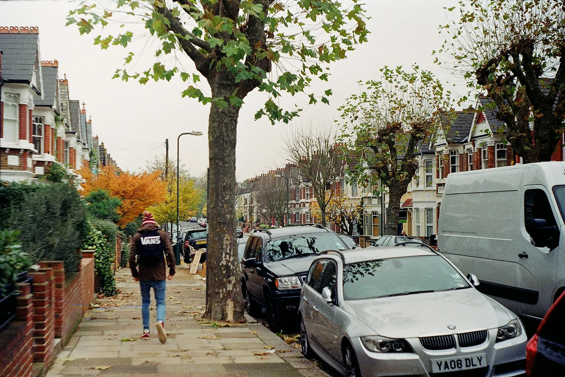 A tree-lined street of red-brick Victorian terraces with bay windows